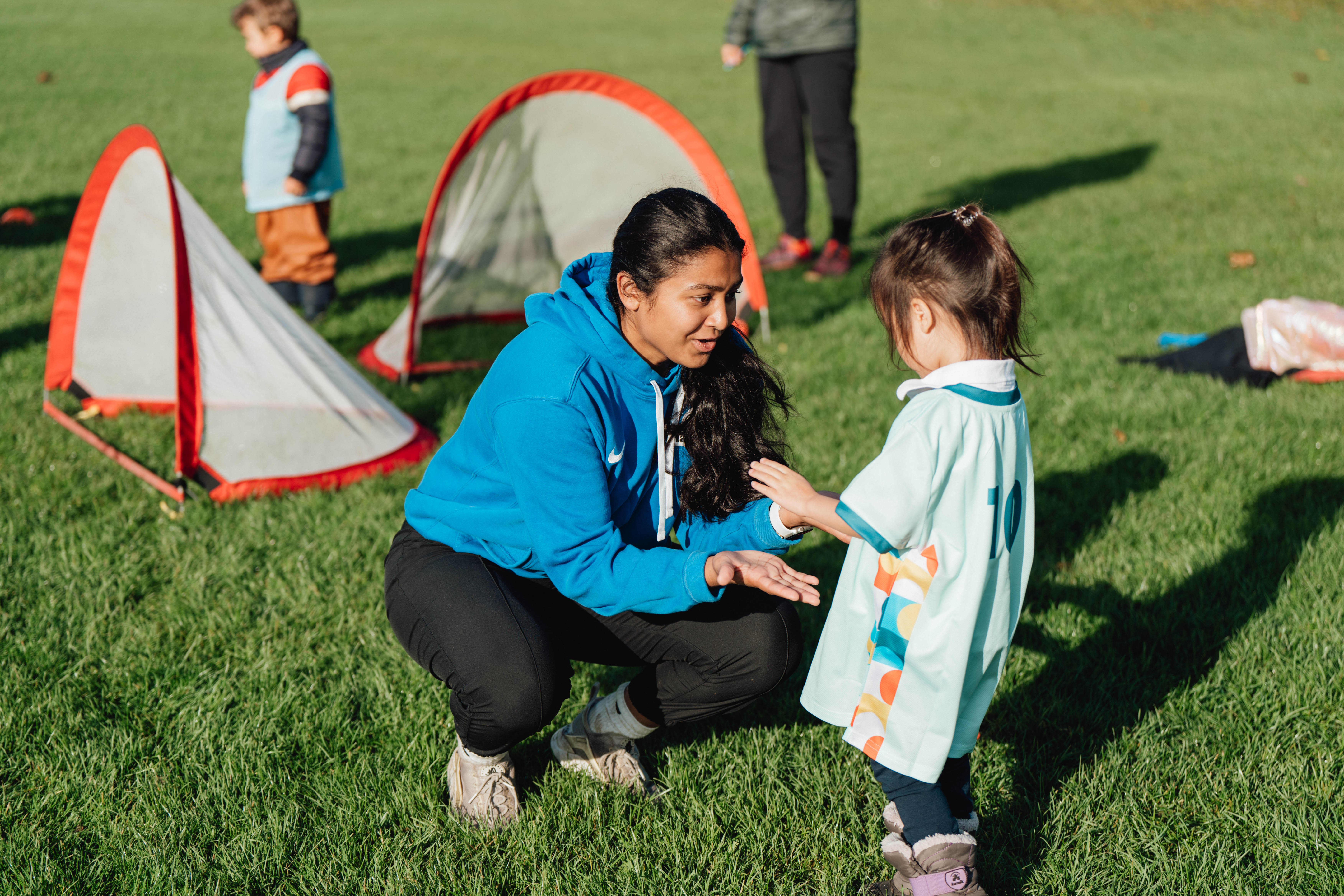 L''entraîneur de soccer de Pedalheads, à genoux, encourage un jeune enfant lors d''un échange individuel sur le terrain.