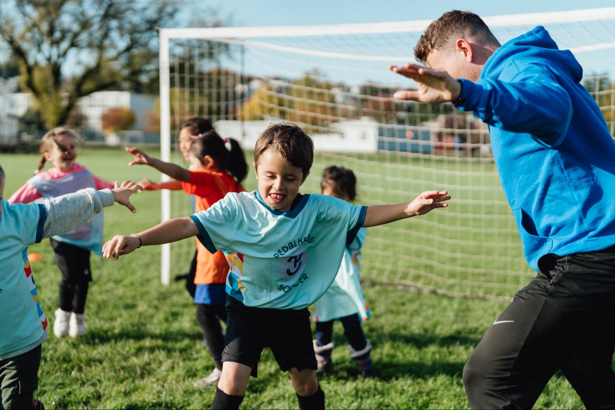 Des enfants s’exercent au soccer sous la supervision d’un entraîneur de Pedalheads sur un terrain extérieur ensoleillé à Toronto.