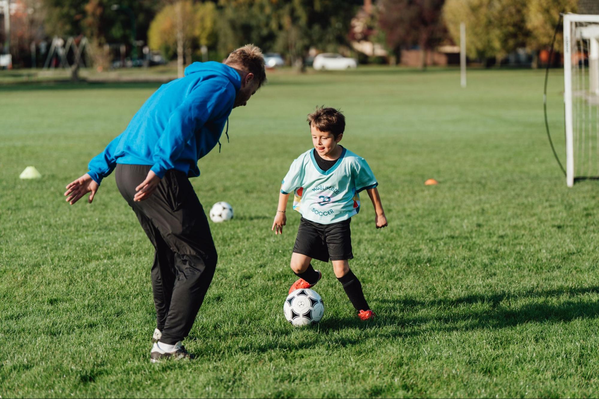 Un jeune joueur de soccer apprend à contrôler le ballon lors d’un cours de Pedalheads avec un entraîneur sur un terrain en gazon.