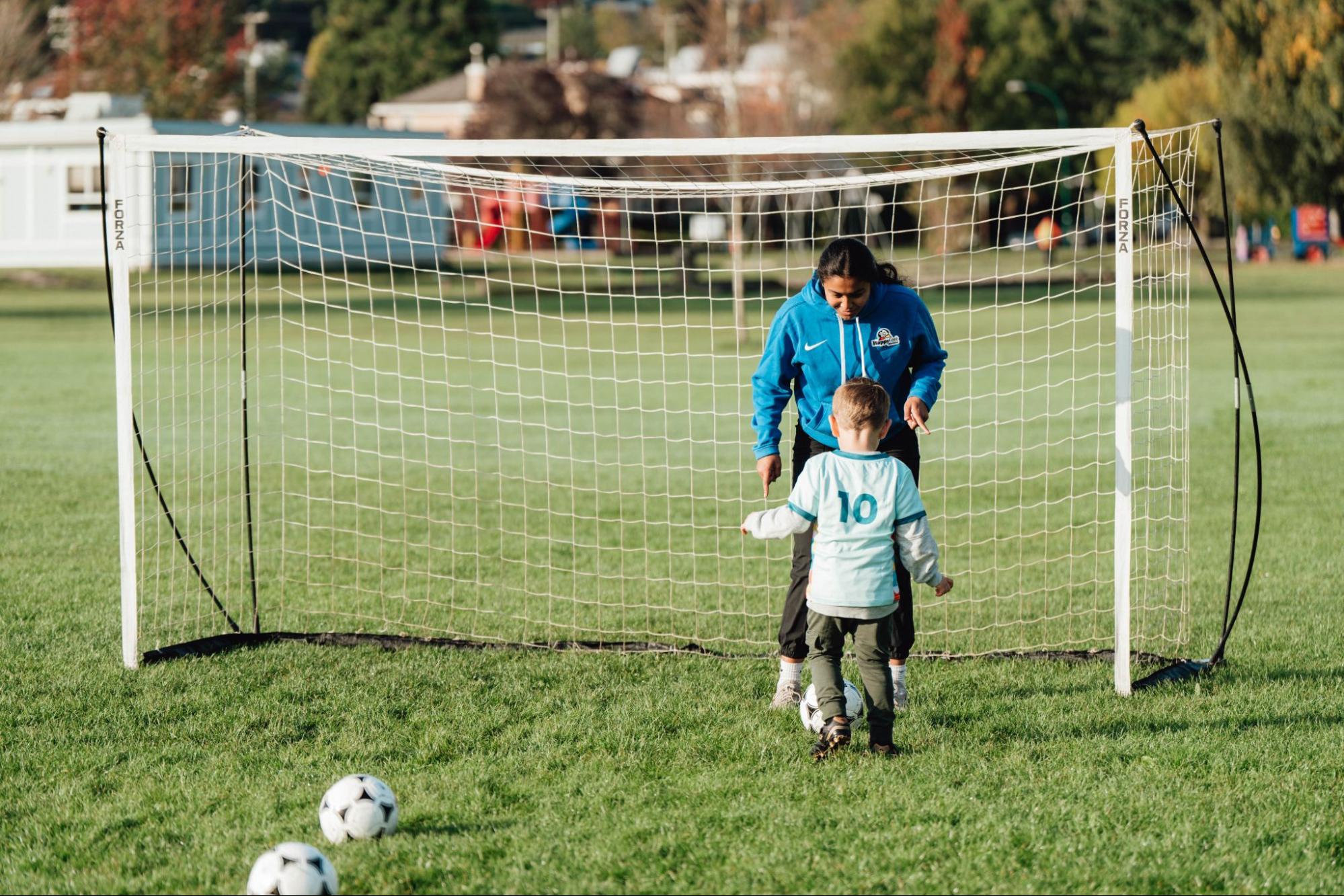 Une entraîneuse de soccer de Pedalheads guide un enfant lors d’un exercice de tir au but en plein air.