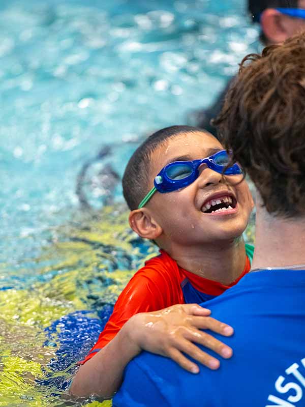 Boy swimming with his instructor and smiling